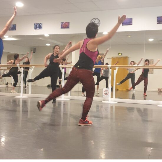cours de cardio fitness dans la salle du Studio Raspail : des femmes sautent vers la droite avec la jambe gauche tendue et la main droite tendue vers le haut