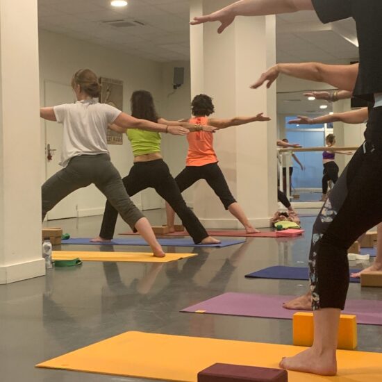 des femmes en posture de yoga du guerrier sur des tapis de sol dans la salle du Studio Raspail